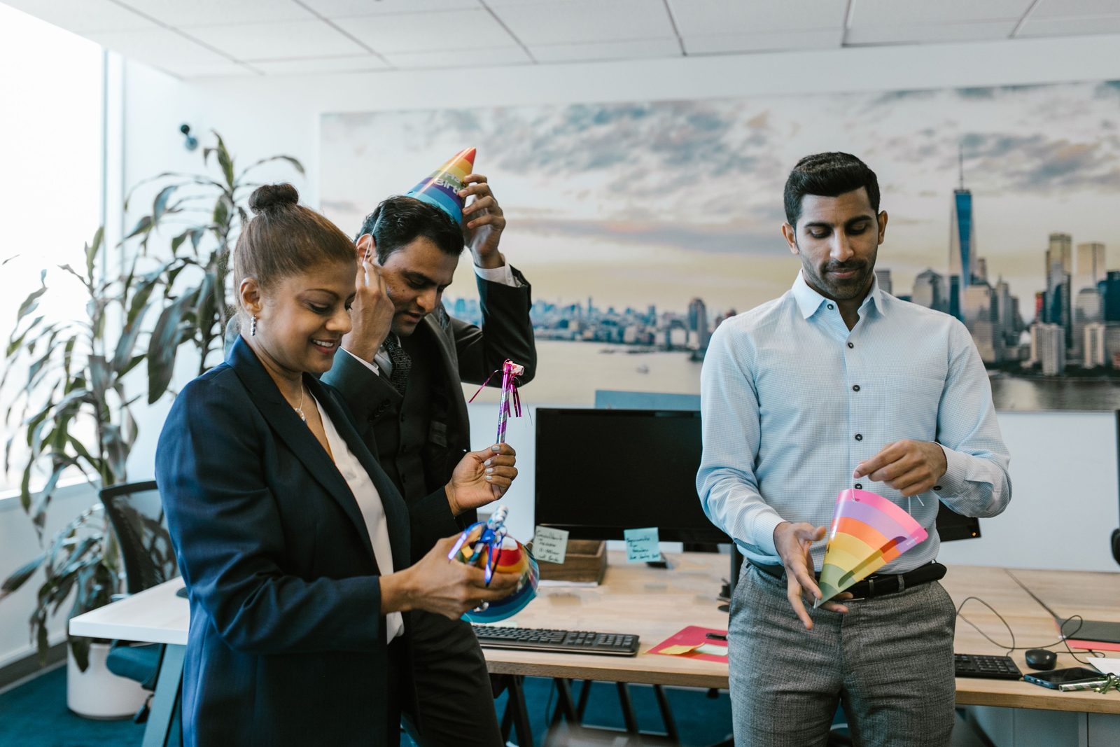 Colleagues in suits preparing rainbow party hats for an office celebration