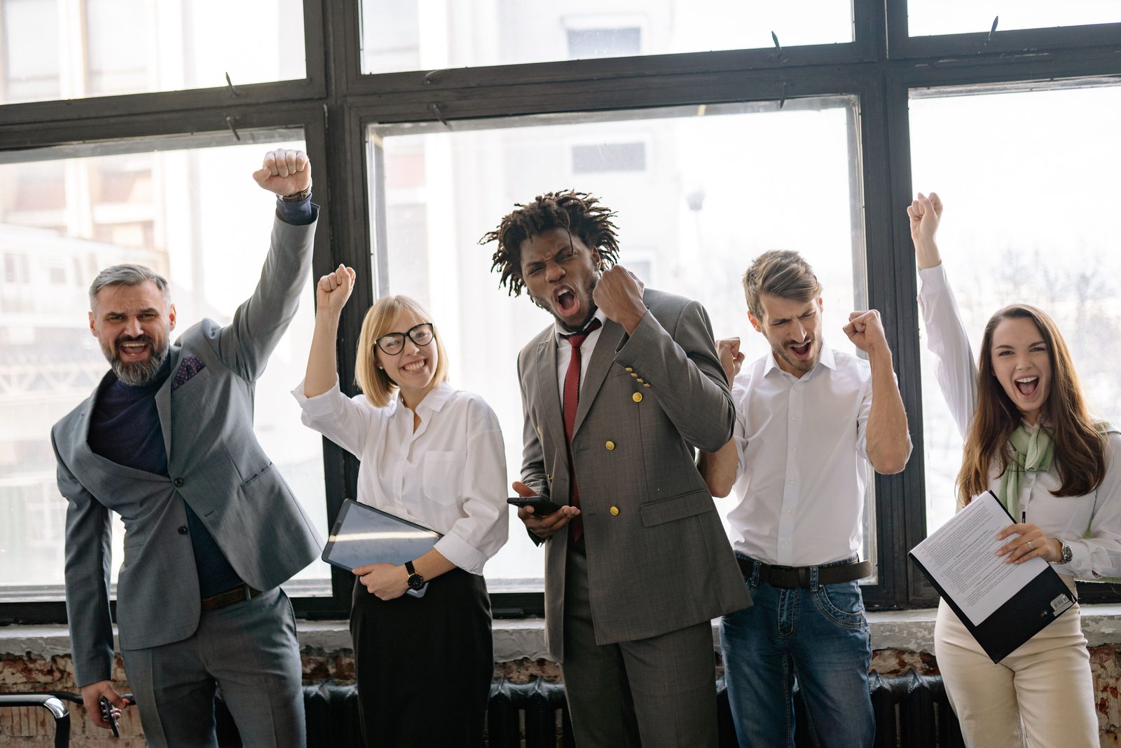 Five coworkers cheering with raised fists in a bright loft office